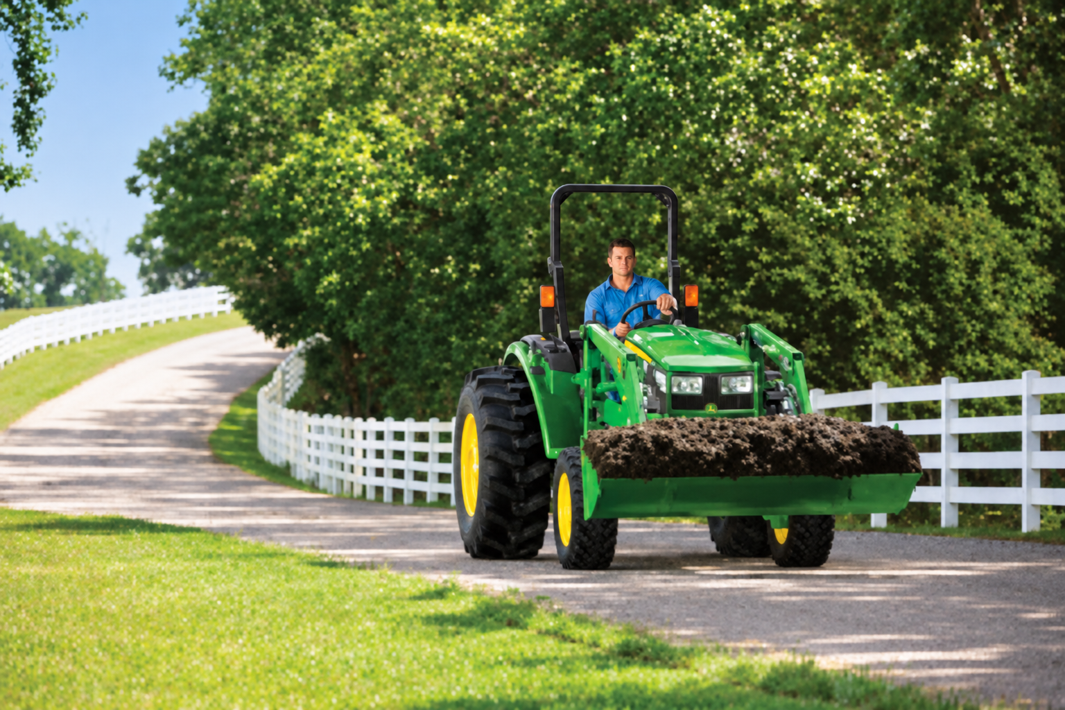 John Deere compact tractor carrying material in its loader bucket