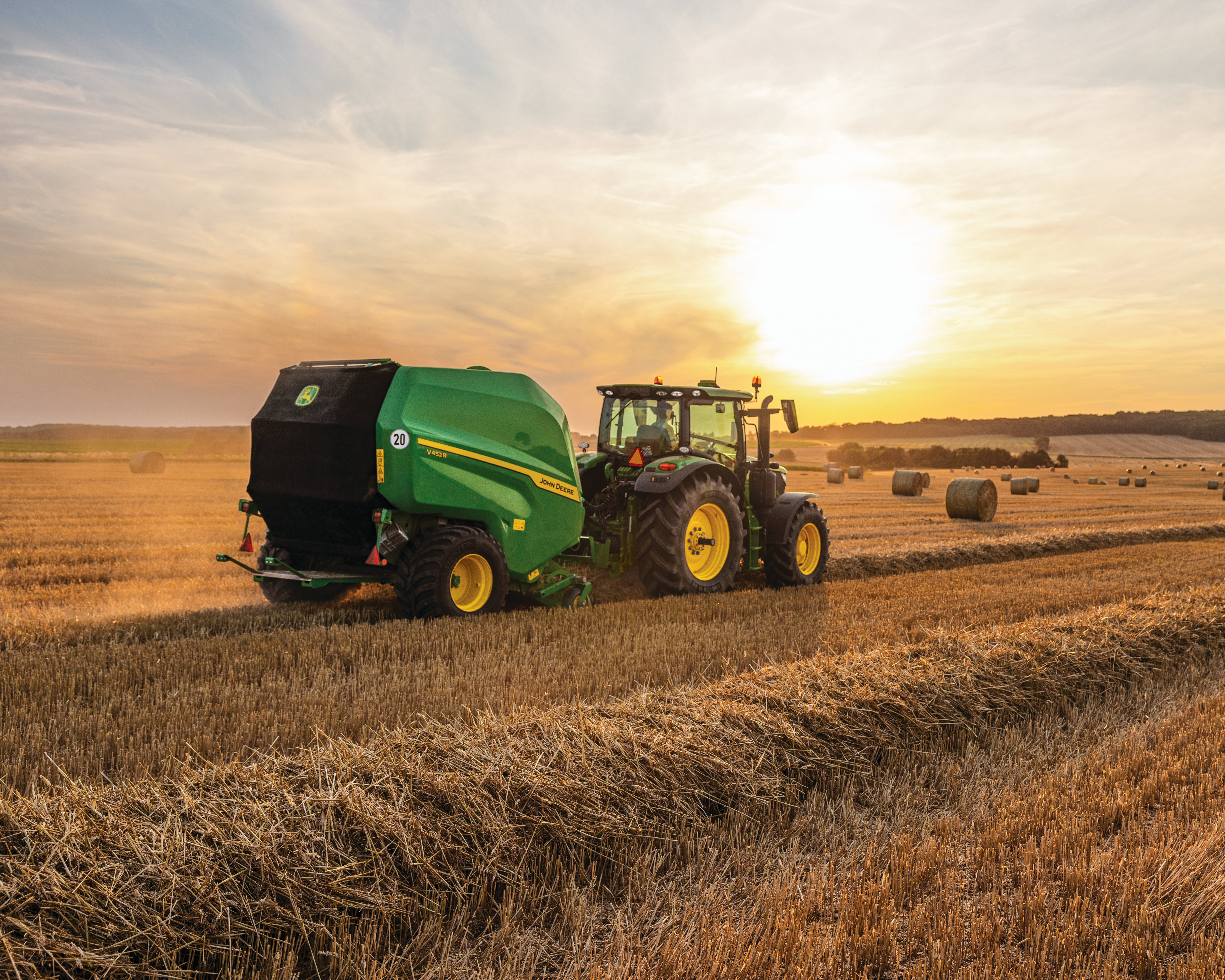 John Deere round baler and tractor at sunset