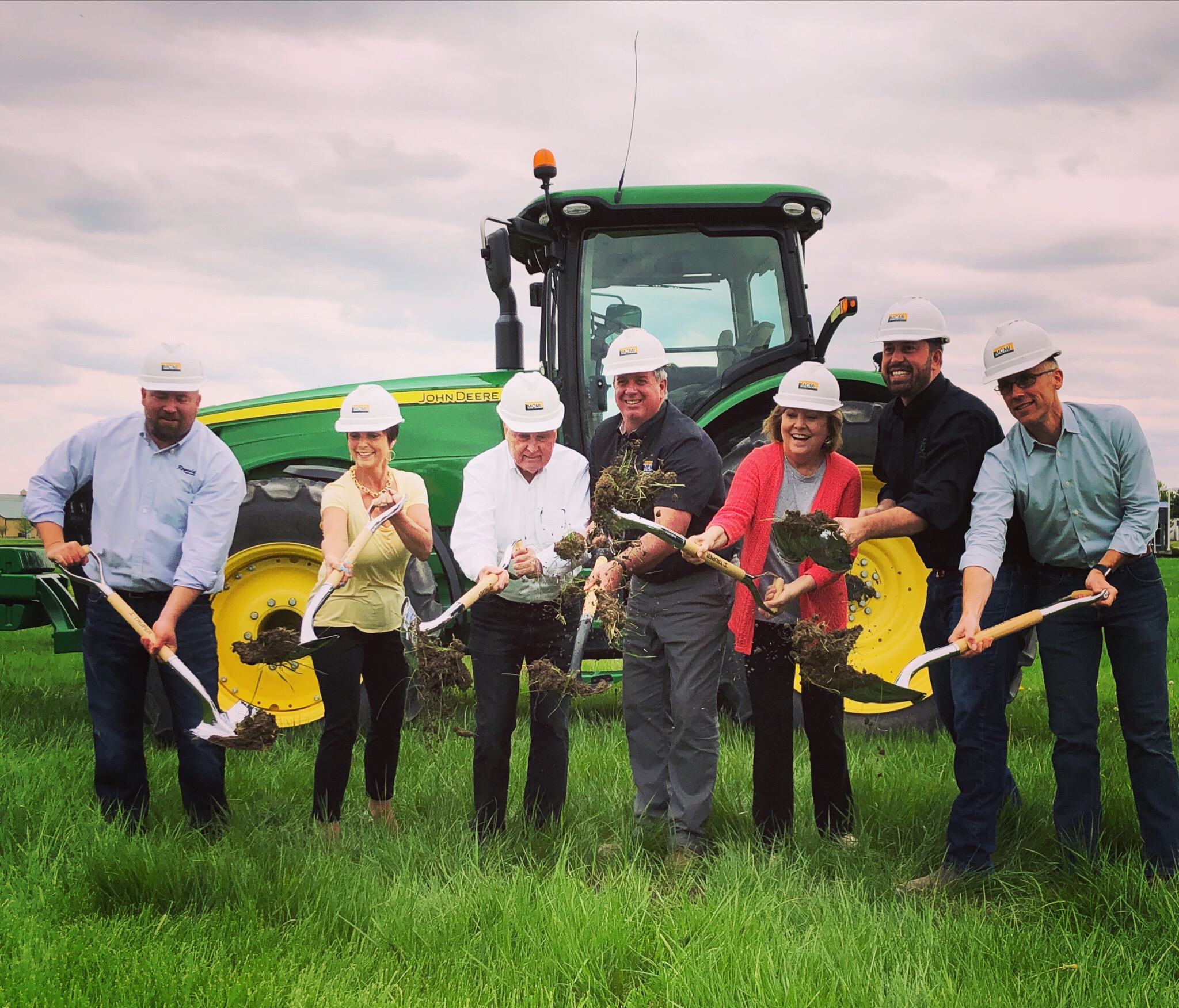 Image is of the Reynolds executive in white hard hats breaking ground at the new location in Lebanon. They have a backdrop of a John Deere agricultural tractor.