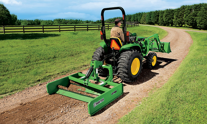 A man is on a John Deere tractor with a Frontier grating attachment to even out the gravel in his driveway. 